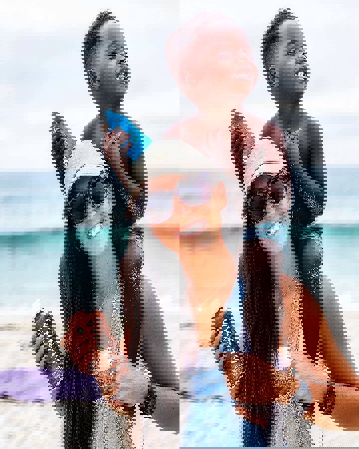 a woman is carrying a child on her shoulders on the beach while holding a bottle of aloha