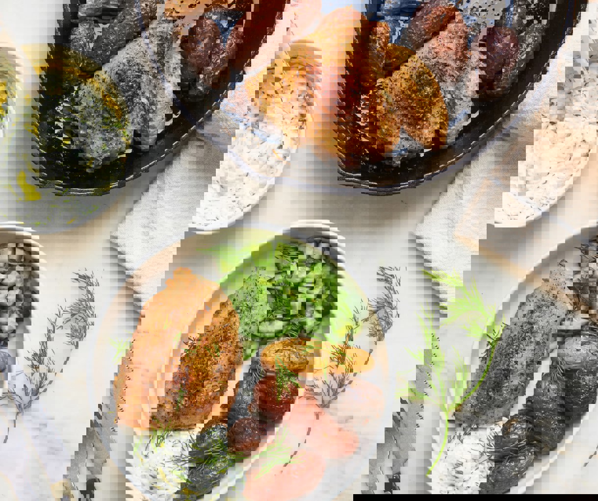 a plate of food with chicken potatoes and cucumbers next to a skillet