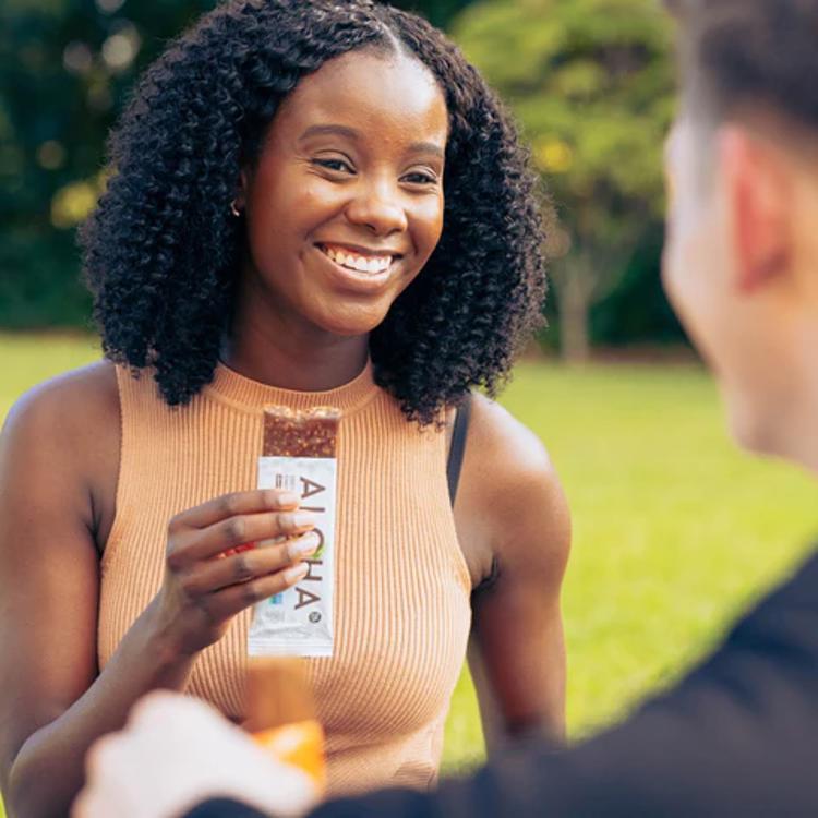 a woman is holding a bar of chocolate and smiling while talking to a man