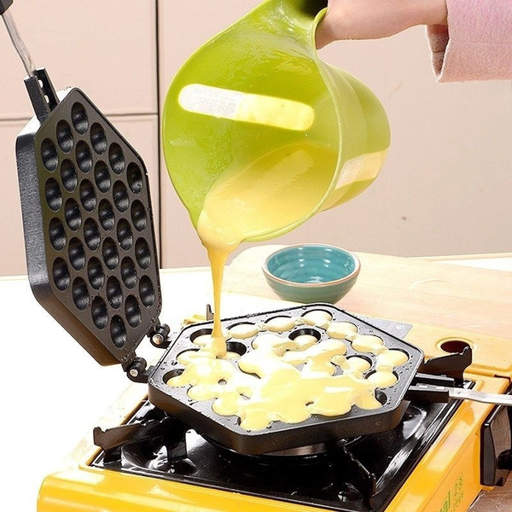 a person pouring batter into a waffle maker on a stove
