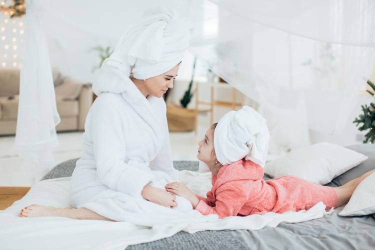 a woman and a little girl are sitting on a bed with towels wrapped around their heads