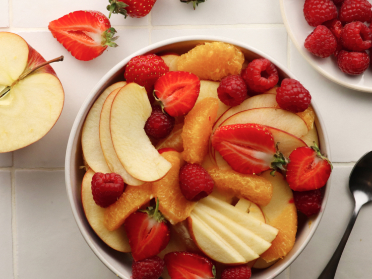 a bowl of fruit including apples raspberries oranges and strawberries