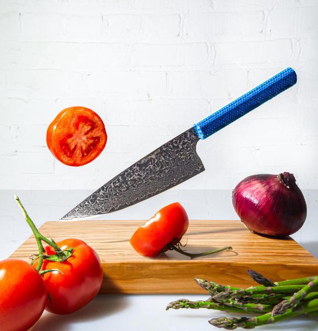 Japanese knife floating in the air over a cutting board with asparagus and tomatoe