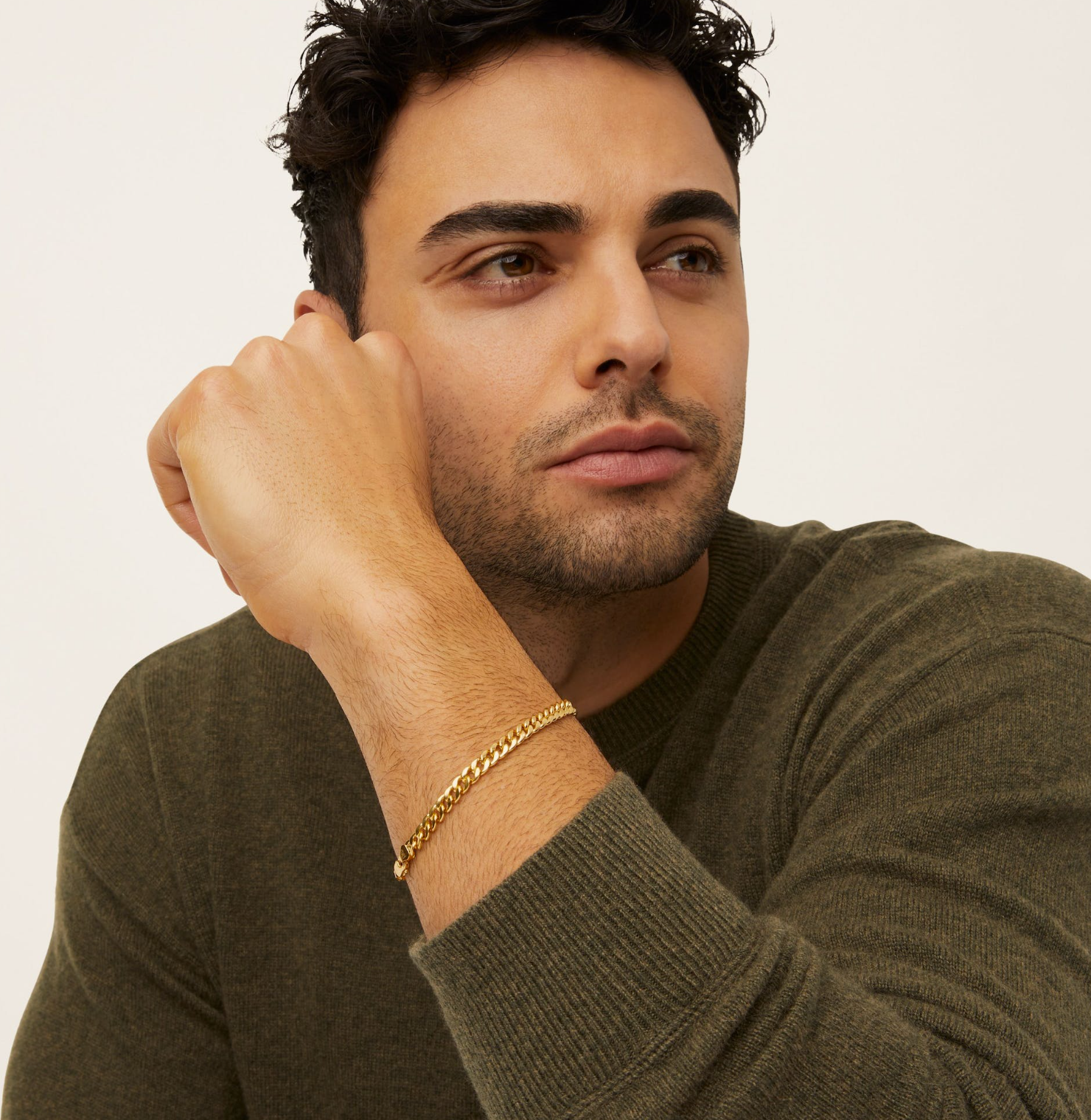 a man wearing a green sweater and a gold bracelet on his wrist
