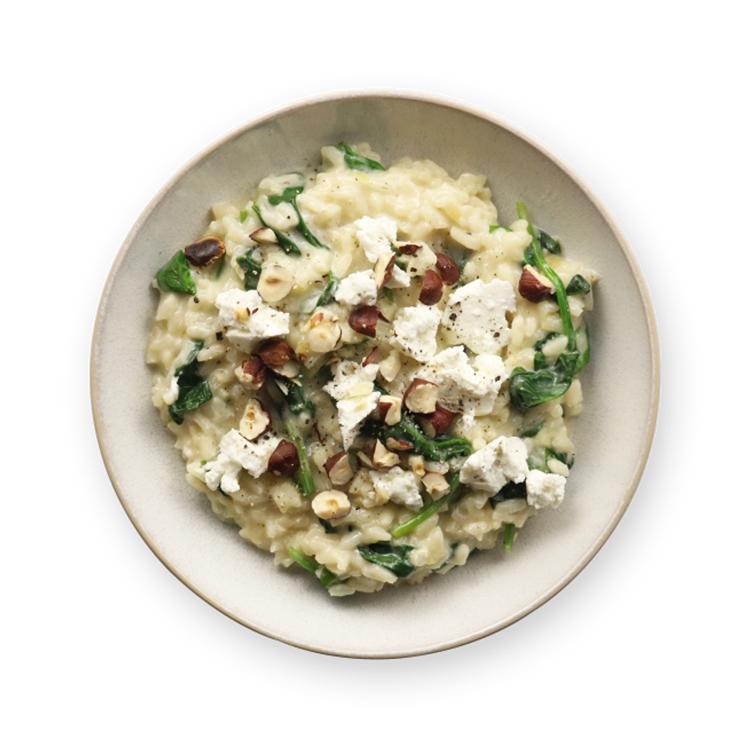 a bowl of risotto with spinach , hazelnuts and feta cheese on a black background