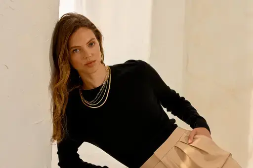 a woman wearing a black sweater and tan pants is leaning against a wall