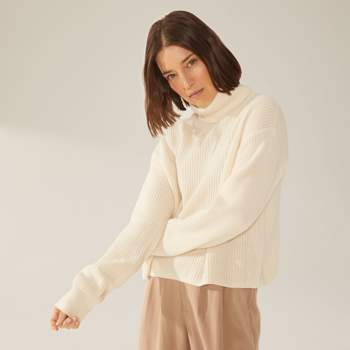 a woman wearing a white sweater and brown pants