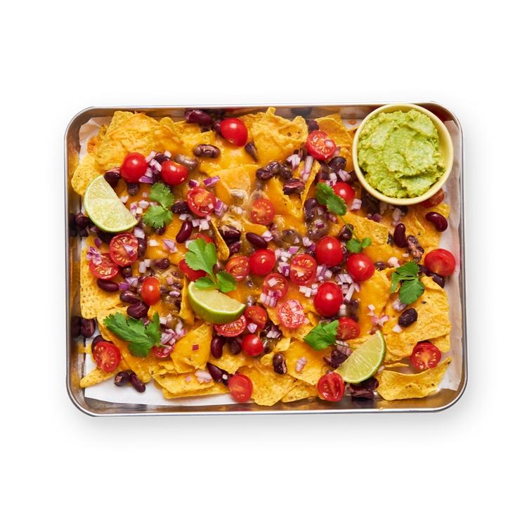a tray of nachos with guacamole and tomatoes on a black background