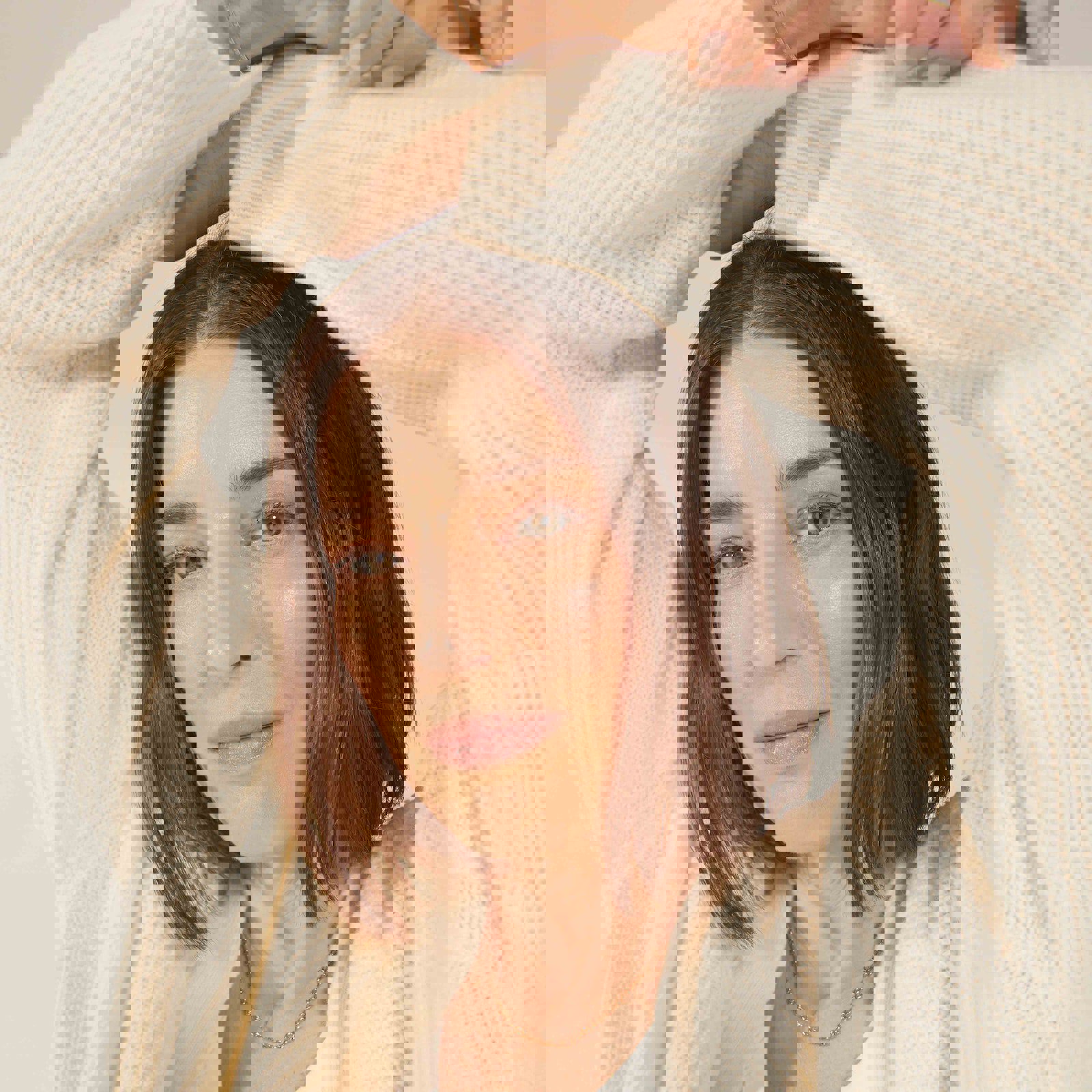 a woman is wearing a white sweater and a gold necklace