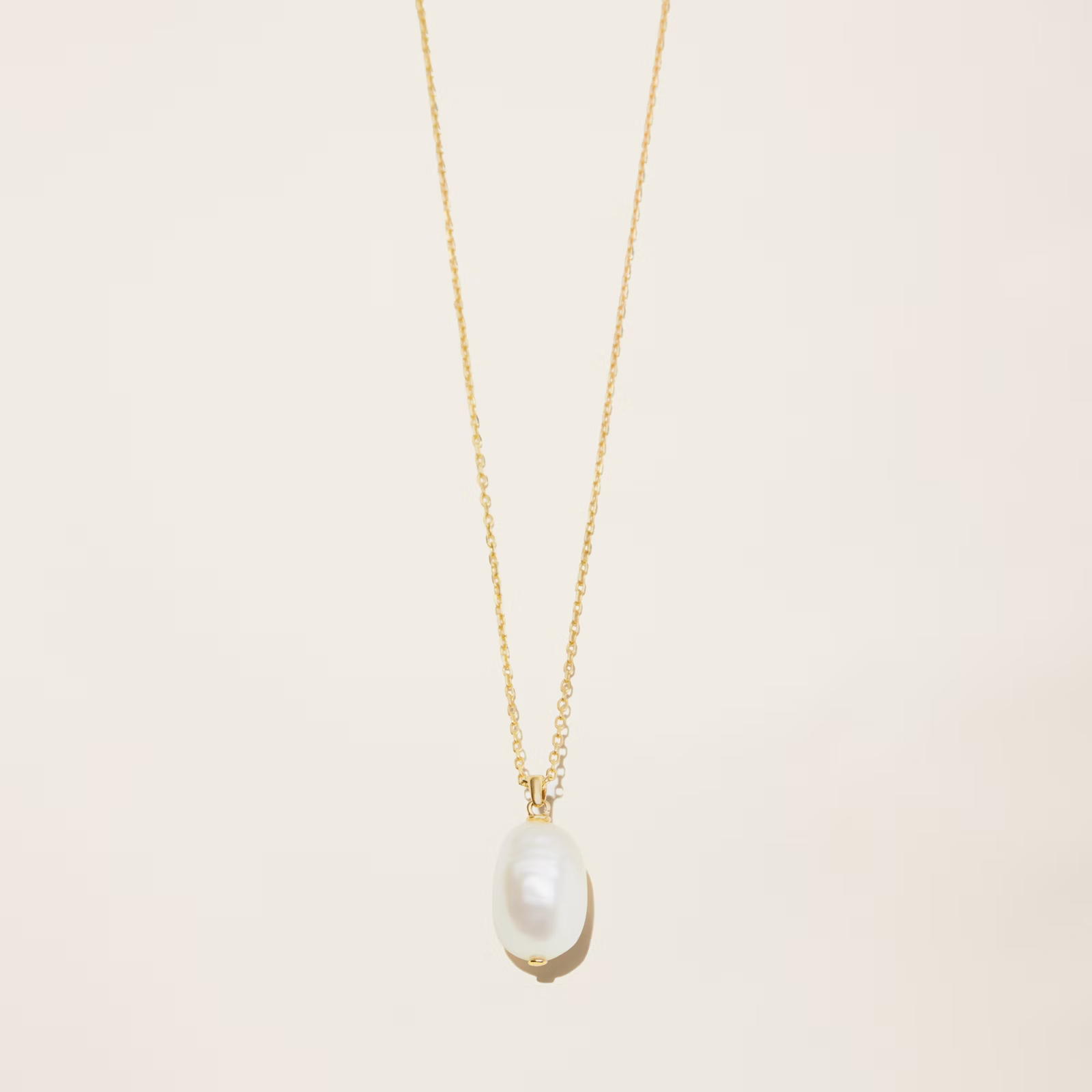 a gold necklace with a pearl pendant on a white surface