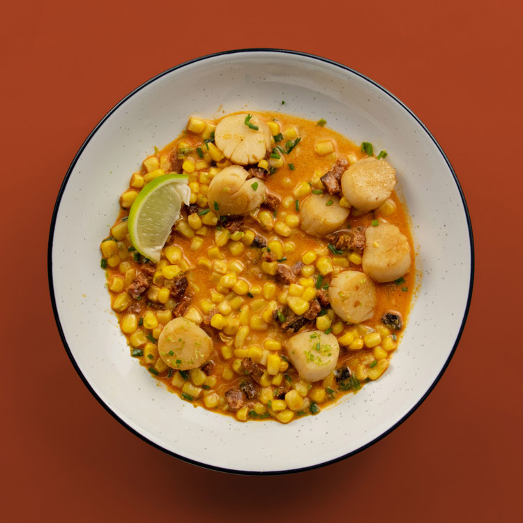 a bowl of corn and scallops on a red background
