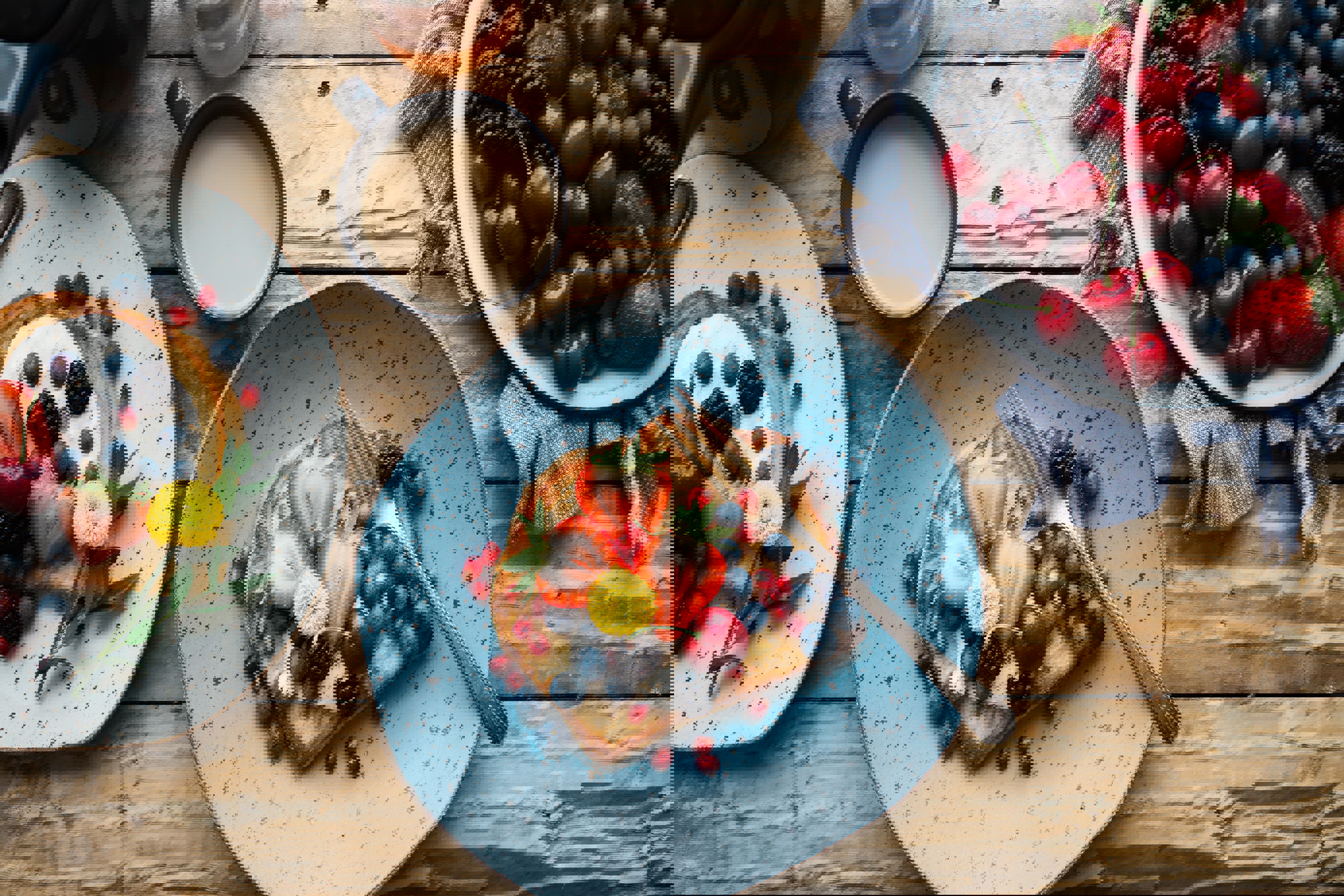 three plates of food with berries and a cup of coffee on a wooden table