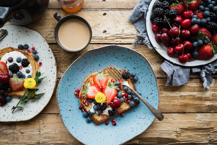 three plates of food with berries and a cup of coffee on a wooden table