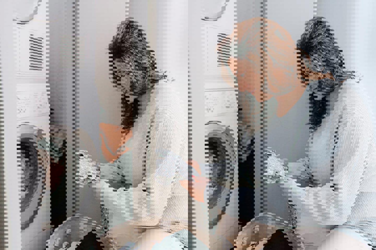 a woman is sitting on the floor looking at clothes in a laundry room