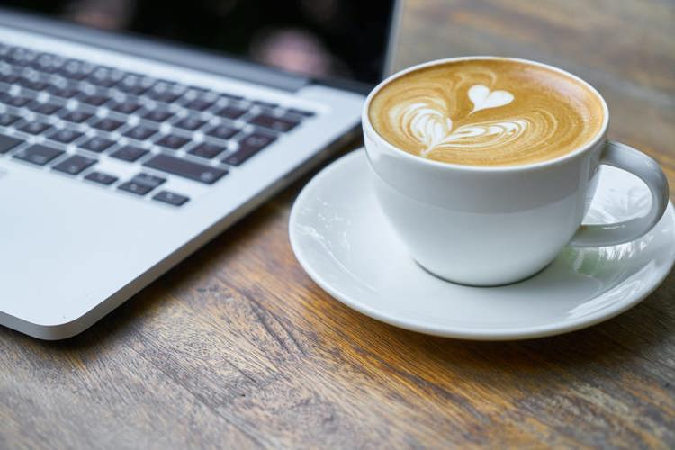 a cup of coffee on a saucer next to a laptop