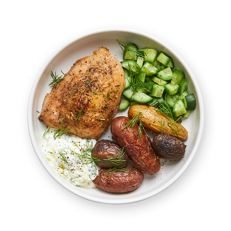 a white plate topped with chicken , potatoes , cucumbers and yogurt sauce