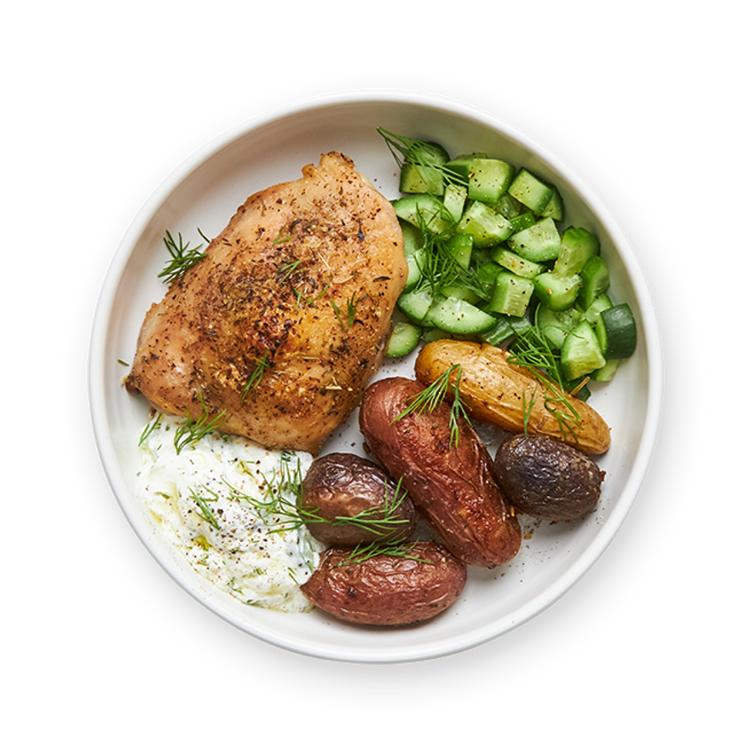 a white plate topped with chicken , potatoes , cucumbers and yogurt sauce