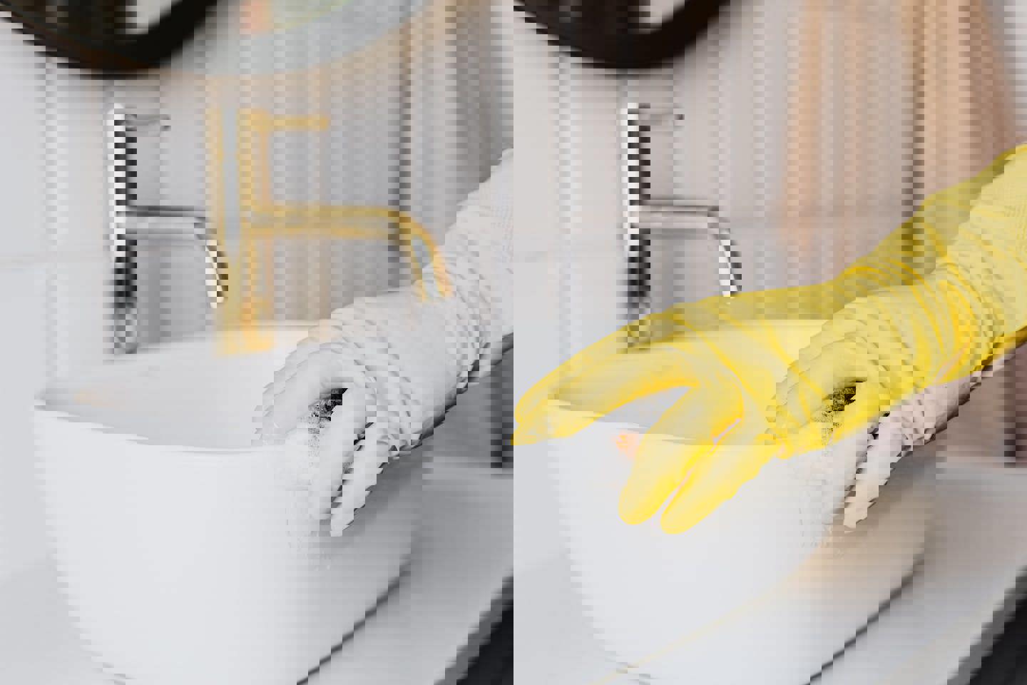 a person wearing yellow gloves is cleaning a bathroom sink with a sponge