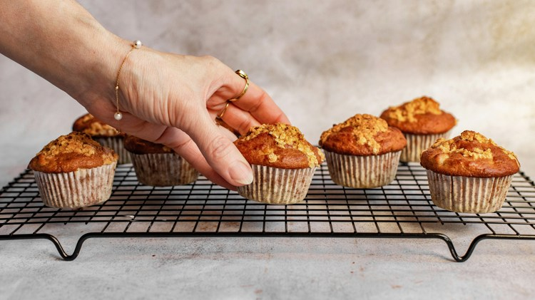 a woman reaches for a cupcake on a cooling rack