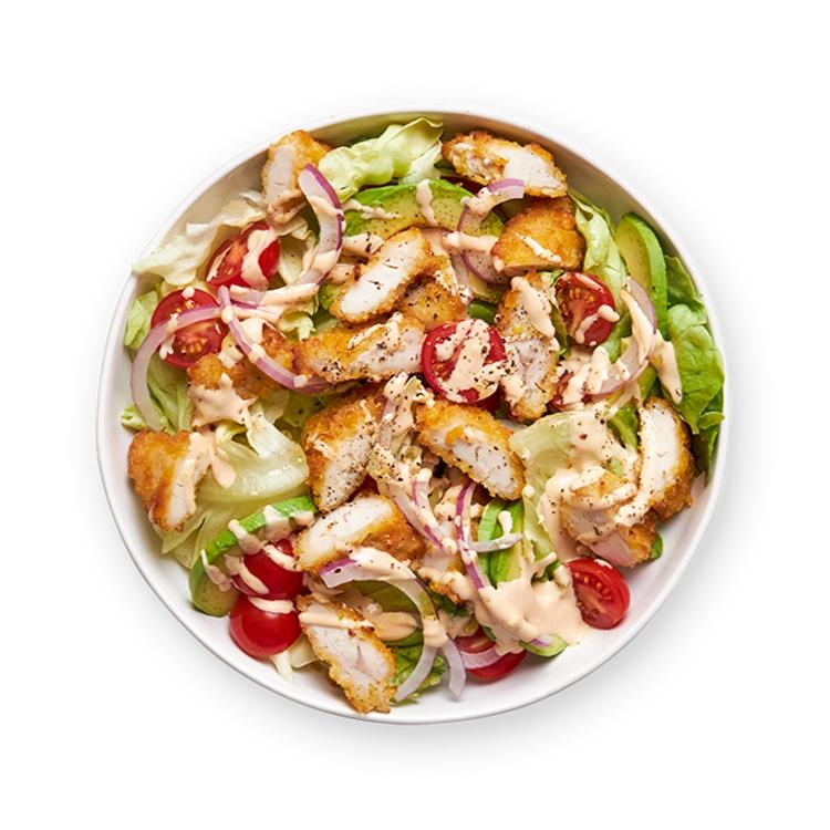 a salad with chicken , lettuce , tomatoes , onions and dressing in a bowl on a black background