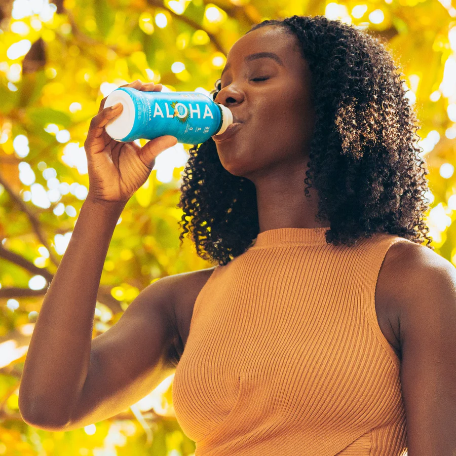 a woman is drinking from a bottle of aloha vanilla protein drink