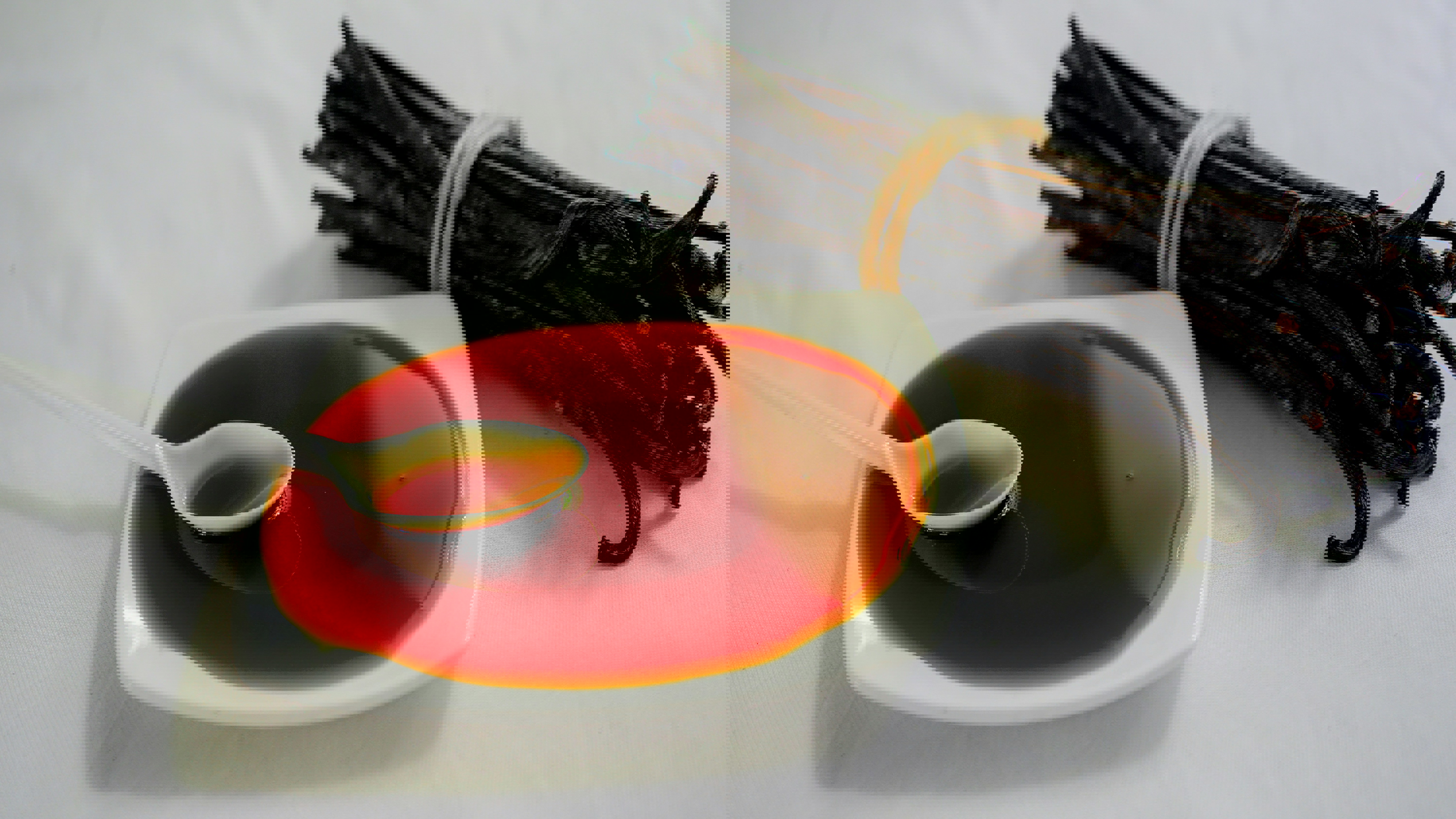 a spoon in a bowl of liquid next to a bunch of vanilla beans