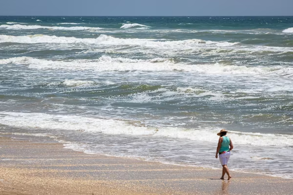 a woman is walking on the beach near the ocean