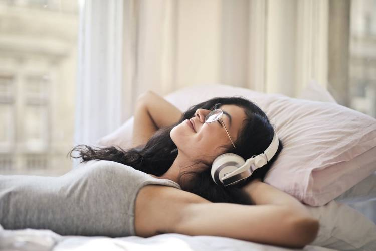 a woman wearing headphones is laying on a bed with her eyes closed