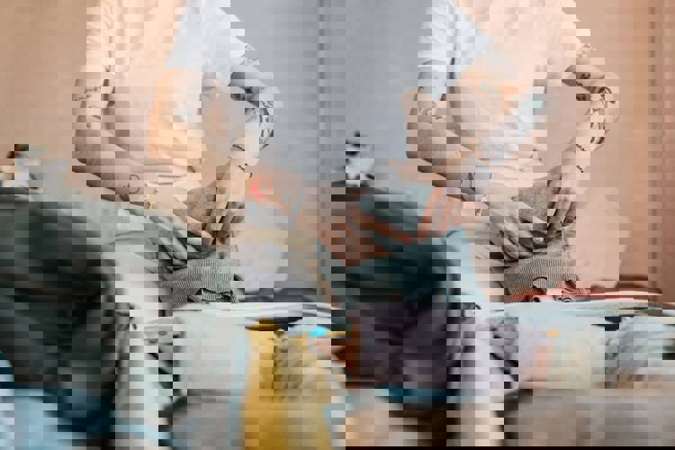 a woman is sitting on a bed packing clothes into a suitcase