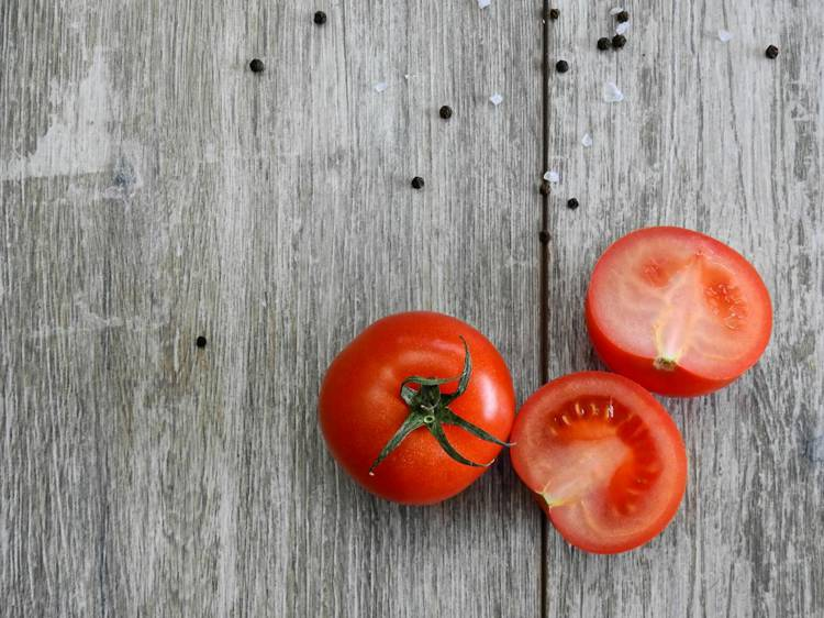 two whole tomatoes and two sliced tomatoes on a wooden table