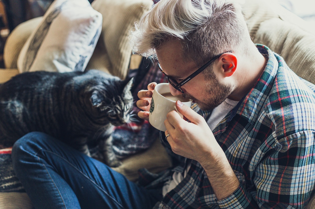 a man drinking a cup of coffee next to a cat