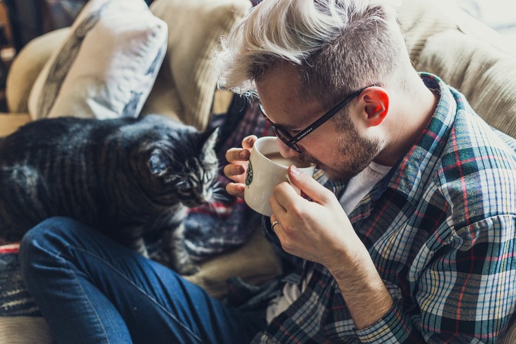 a man drinking a cup of coffee next to a cat