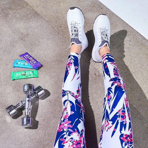 a woman wearing floral leggings and white sneakers is standing next to a pair of dumbbells