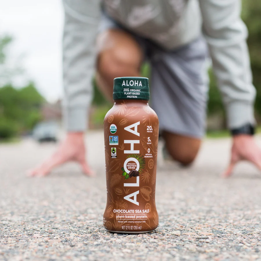 a man is kneeling down in front of a bottle of aloha protein drink