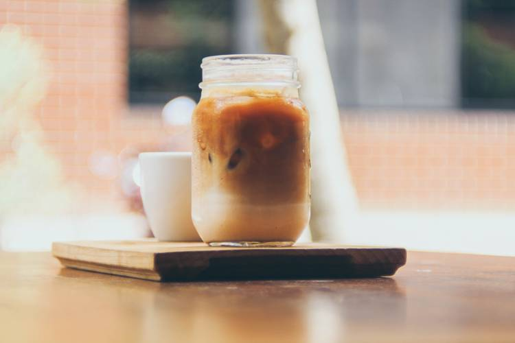 a jar of iced coffee sits on a wooden tray