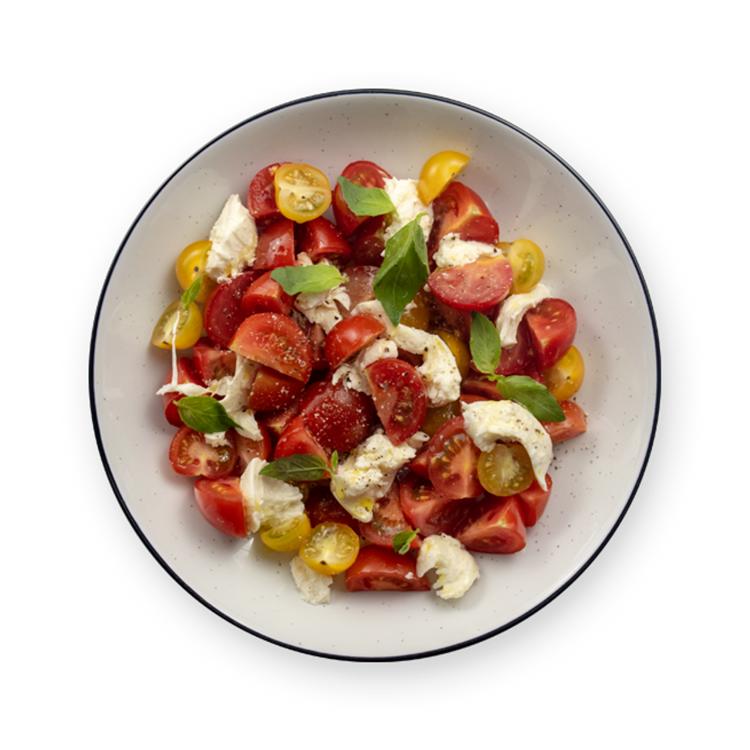 a white bowl filled with tomatoes , mozzarella and basil on a black background