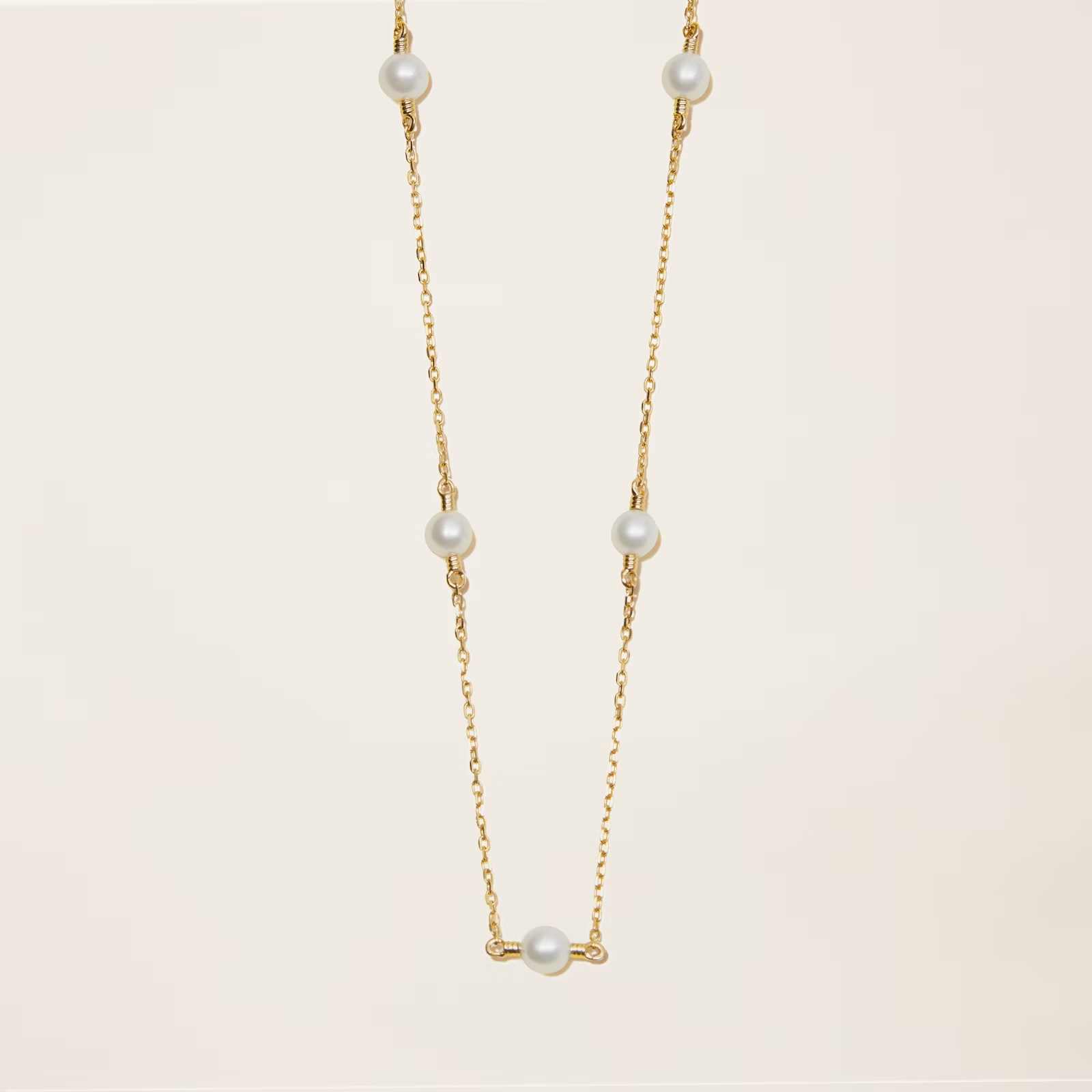 a gold necklace with white pearls on a chain on a white background