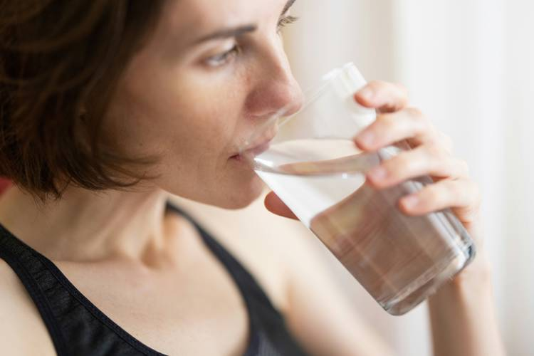 a woman is drinking a glass of water from a clear glass