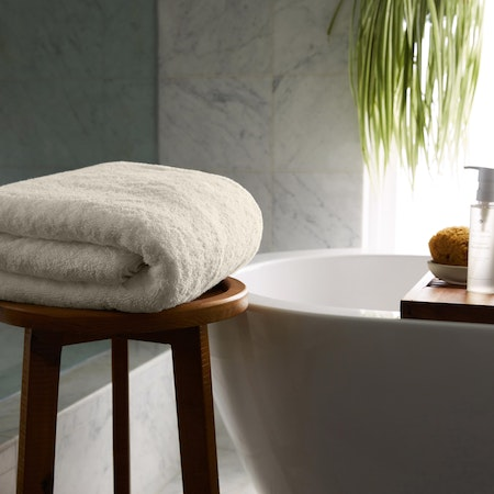 a white towel is sitting on a wooden stool next to a bathtub