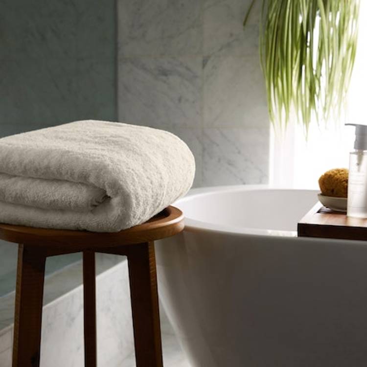 a white towel is sitting on a wooden stool next to a bathtub
