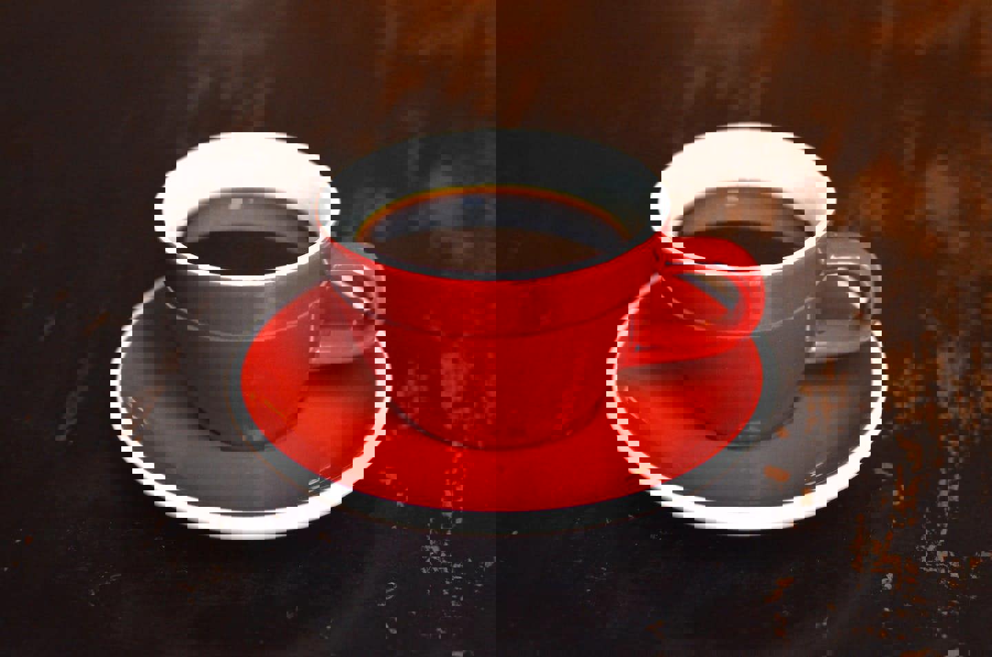 a red cup of coffee on a saucer on a table