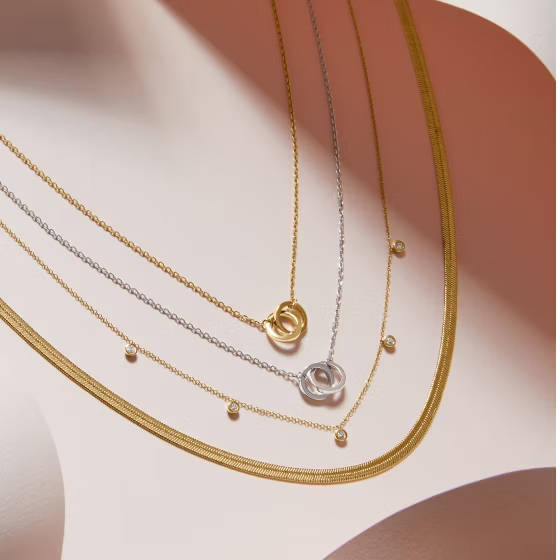 three 14k gold necklaces are stacked on top of each other on a pink surface