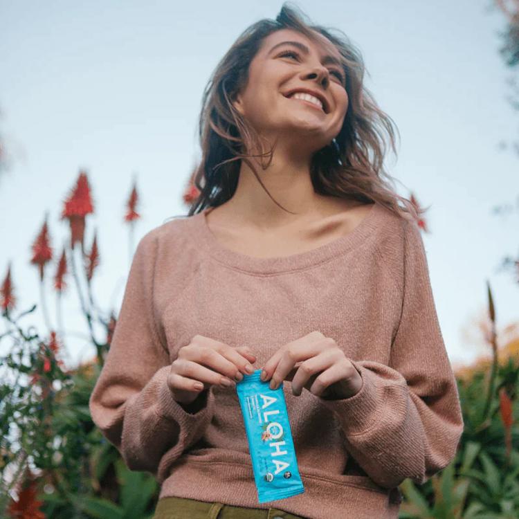 a woman in a pink sweater is holding a blue aloha bar in her hands