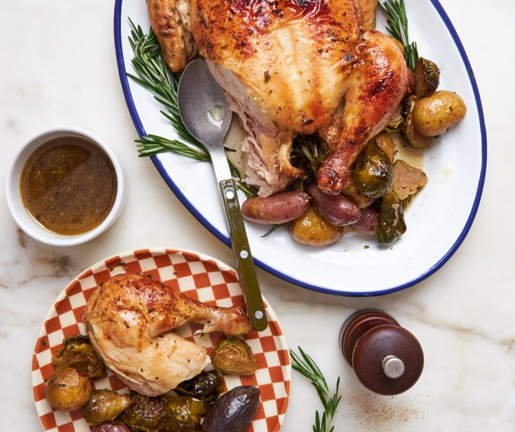 a roasted chicken with potatoes and brussels sprouts on a checkered plate
