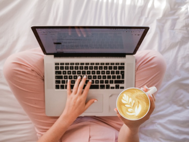 a woman is typing on a laptop while holding a cup of coffee