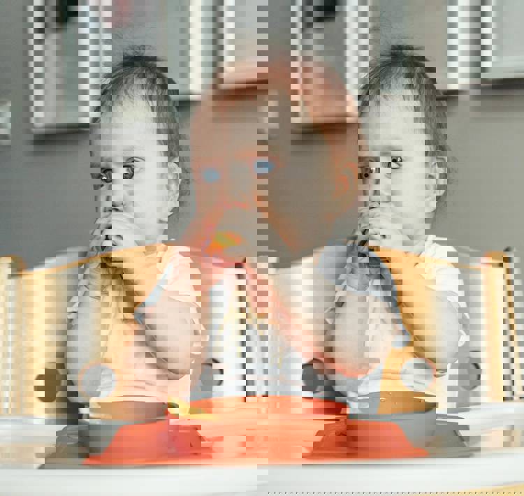 a baby is sitting in a high chair eating an orange