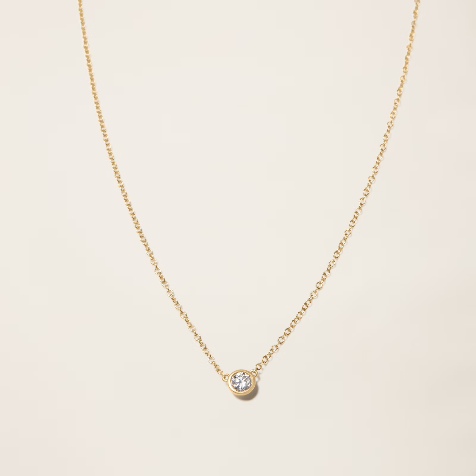 a close up of a gold necklace with a diamond pendant on a white surface