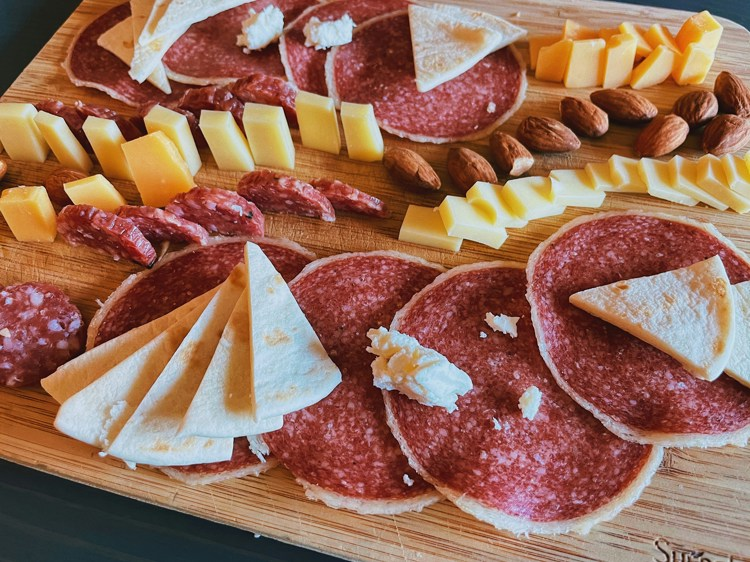 a wooden cutting board with slices of salami cheese and nuts