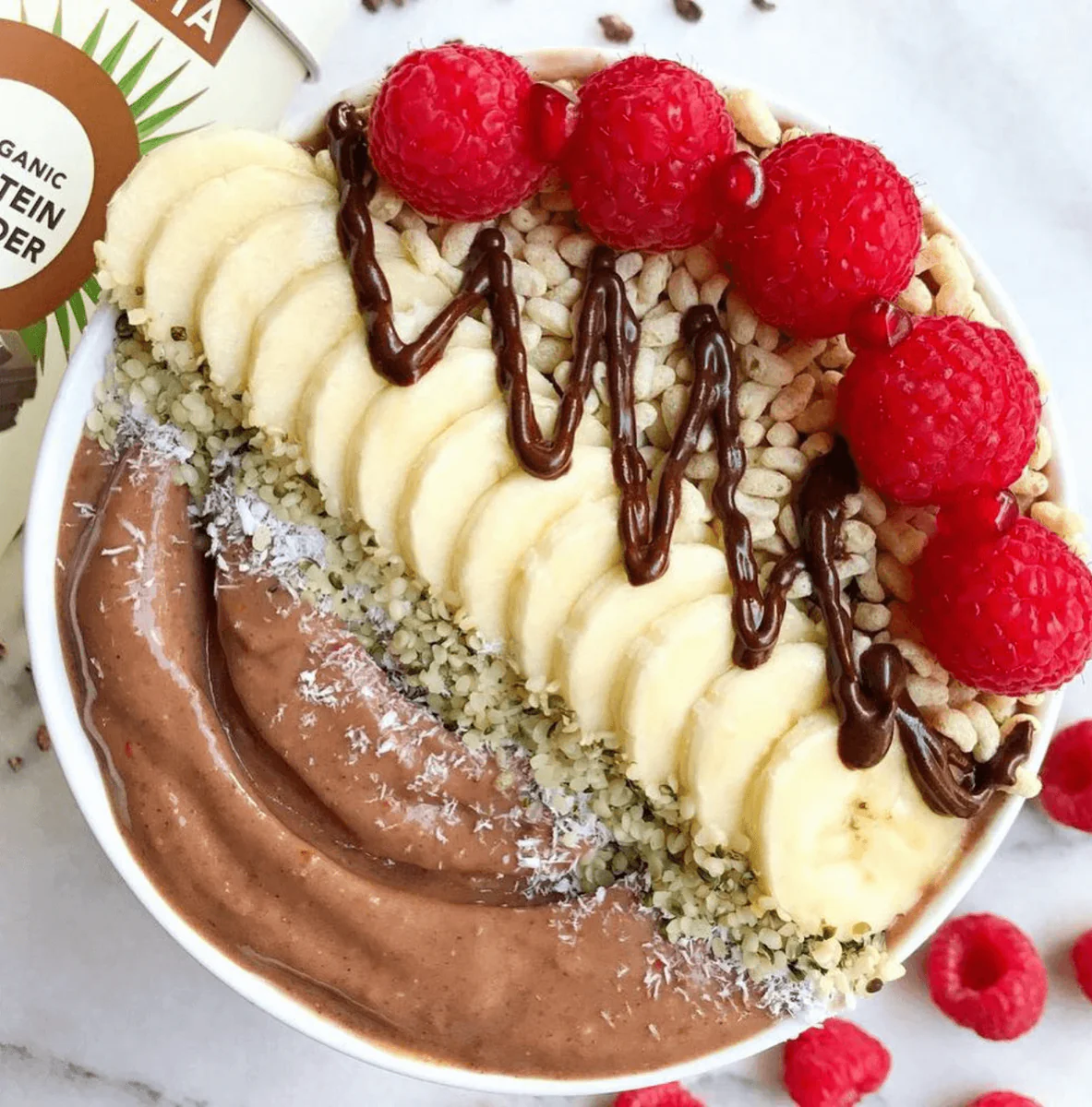 a bowl of chocolate smoothie with bananas and raspberries on top