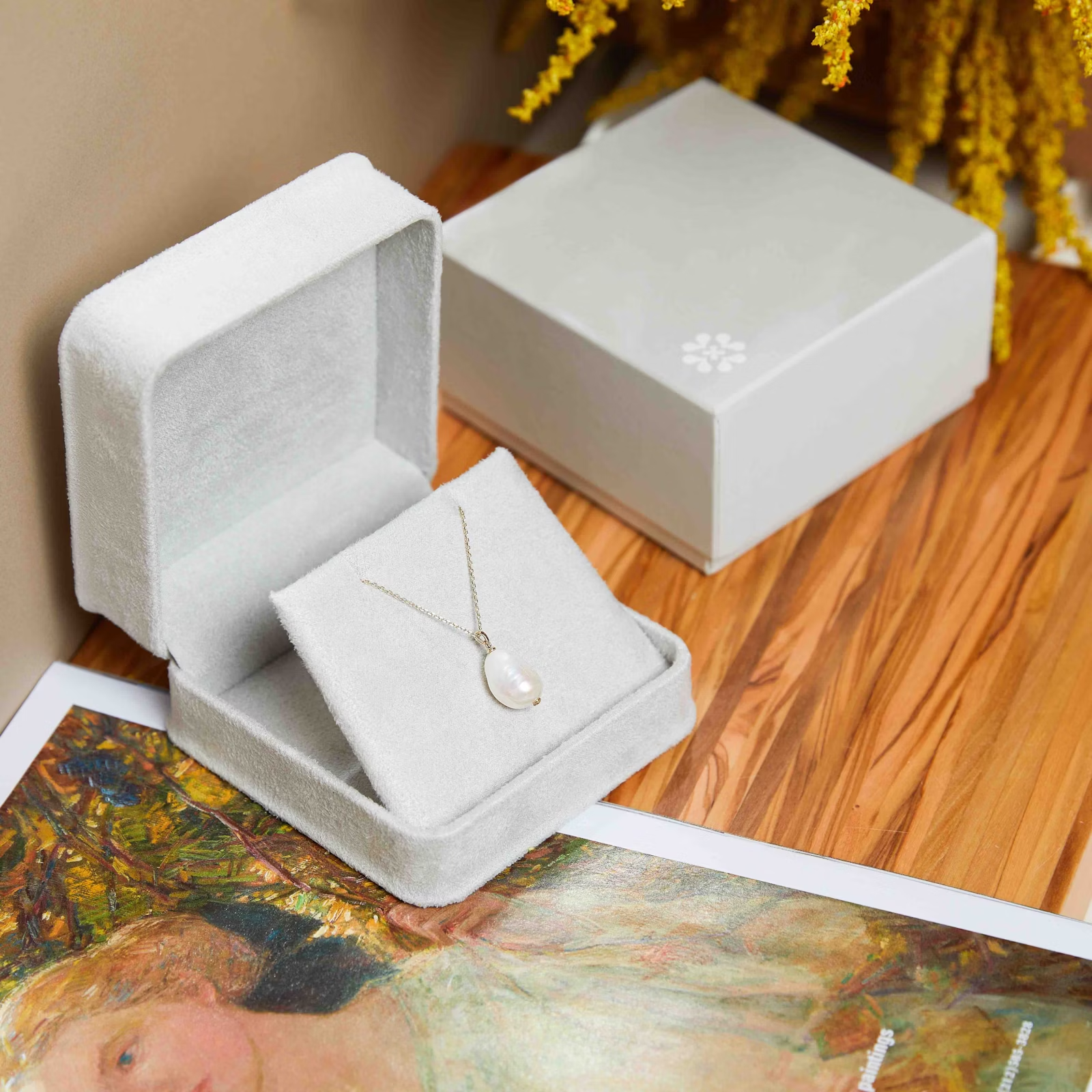 a necklace is in a white box on a wooden table next to a painting